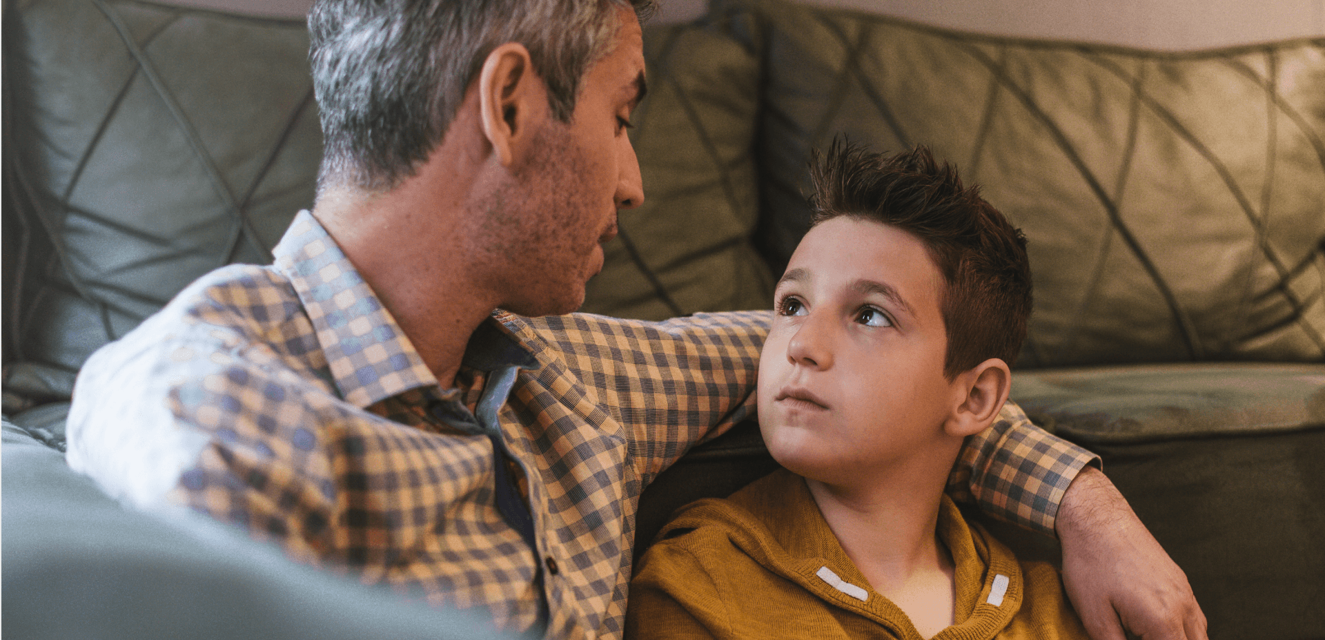elementary-aged boy sitting on the floor next to dad looking up at him and listening to him talk