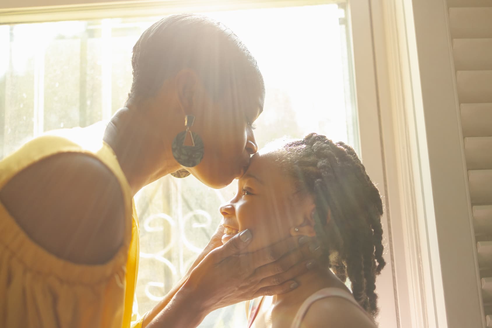 Mother kissing daughter standing by window