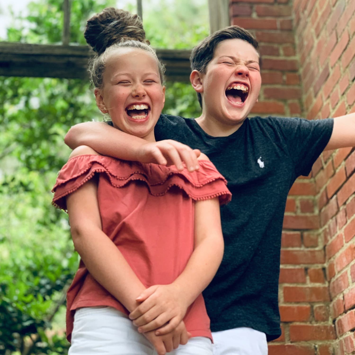 A girl and boy laughing with eyes closed and the boy's arm over the girl's shoulder