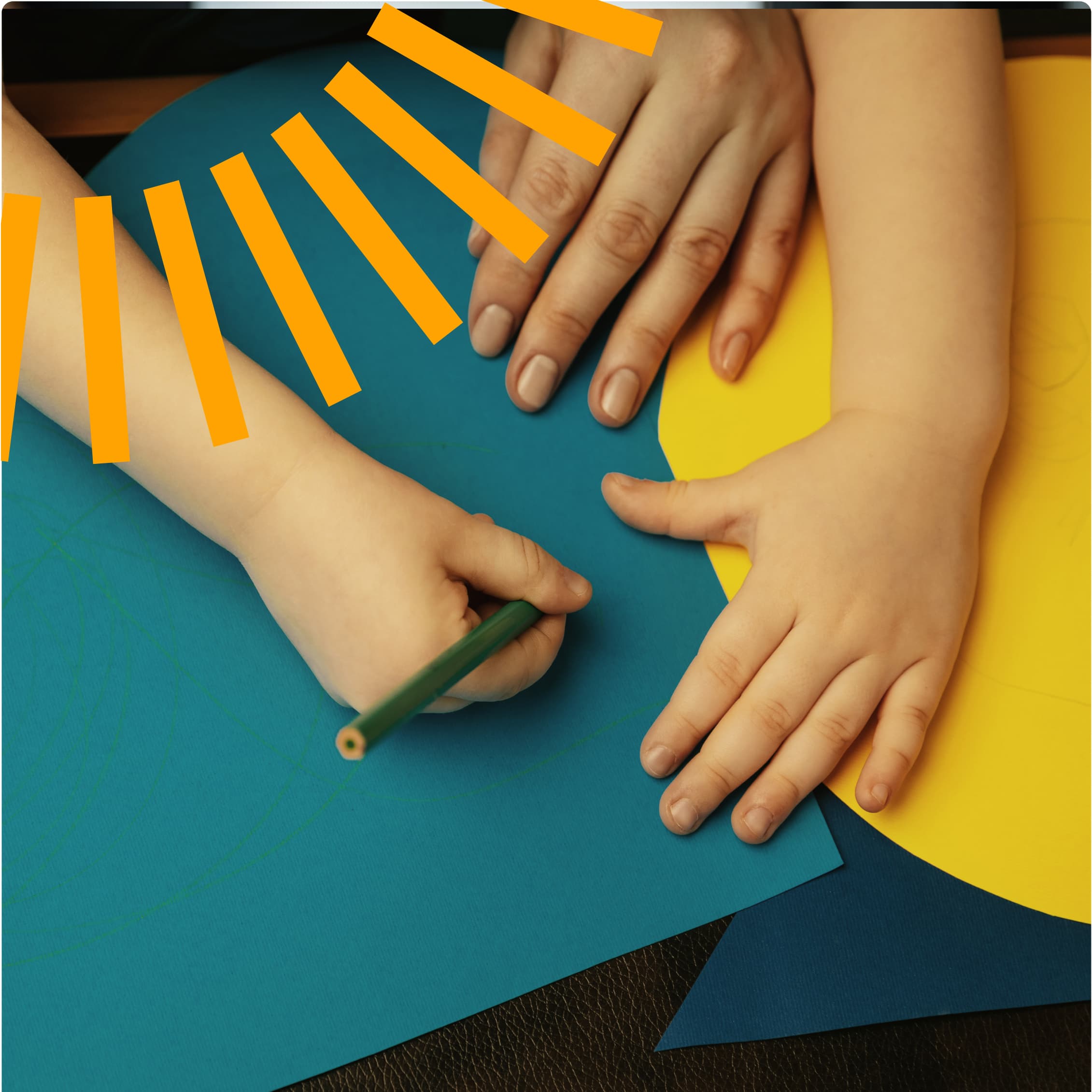 Overhead view of small hands working on a paper craft project, cutting orange strips arranged like sun rays on a turquoise blue background with yellow accent pieces, demonstrating creative children's arts and crafts activity