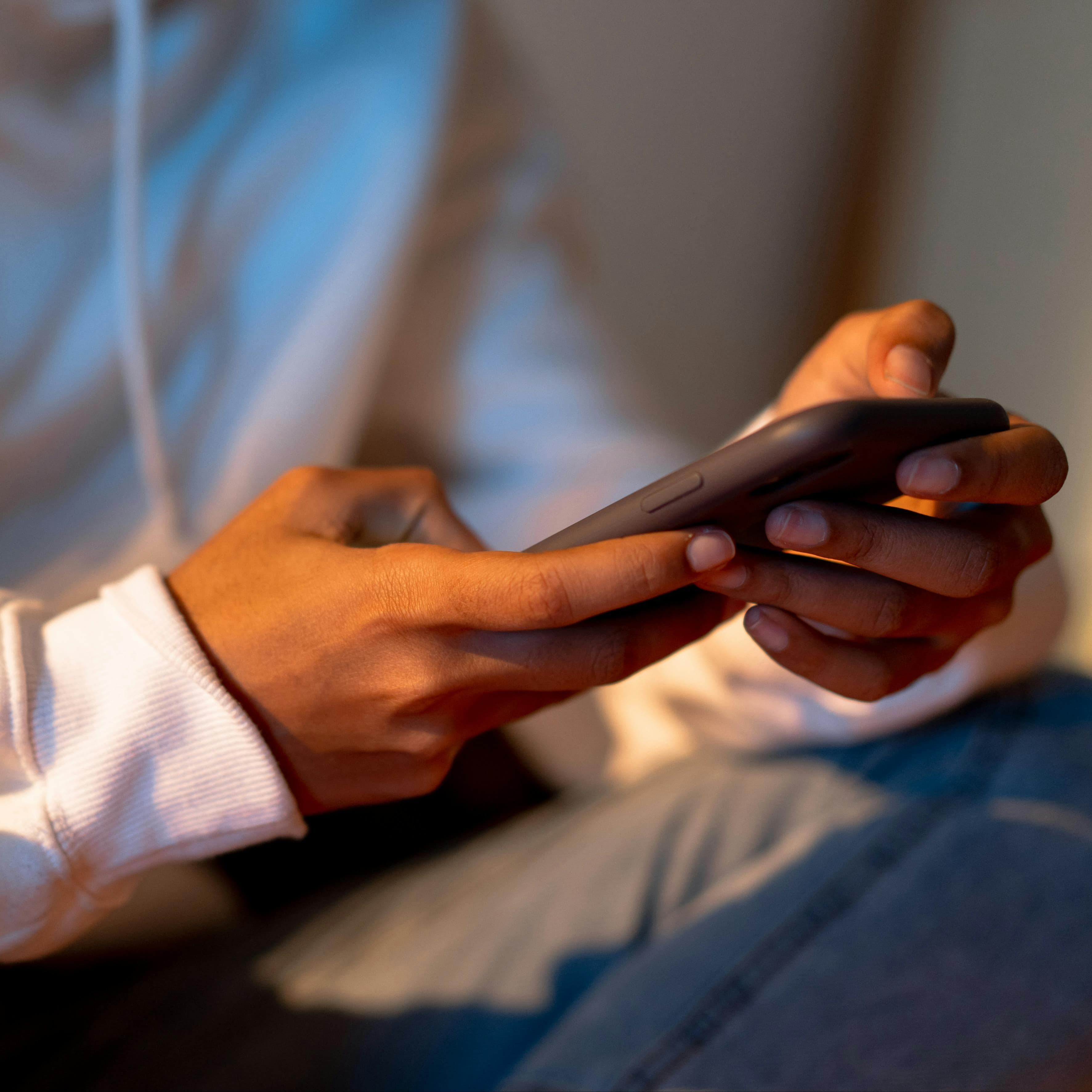 Two teen hands holding a phone and sitting wearing jeans and a hoodie