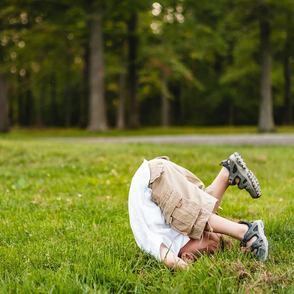 Young boy upside down mid-somersault in a big grassy area with trees in the background
