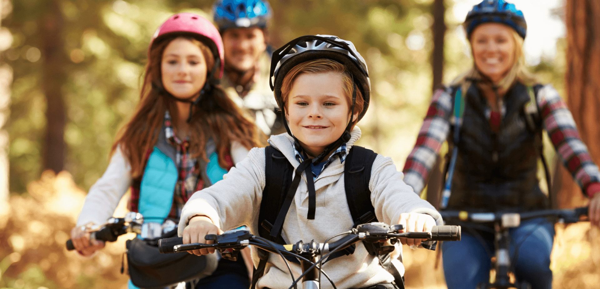 Young boy, older girl, parents in the background all riding bikes outside